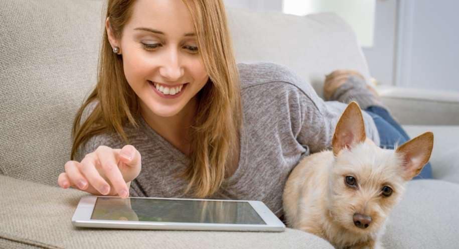 A smiling lady using a tablet device at home alongside her dog