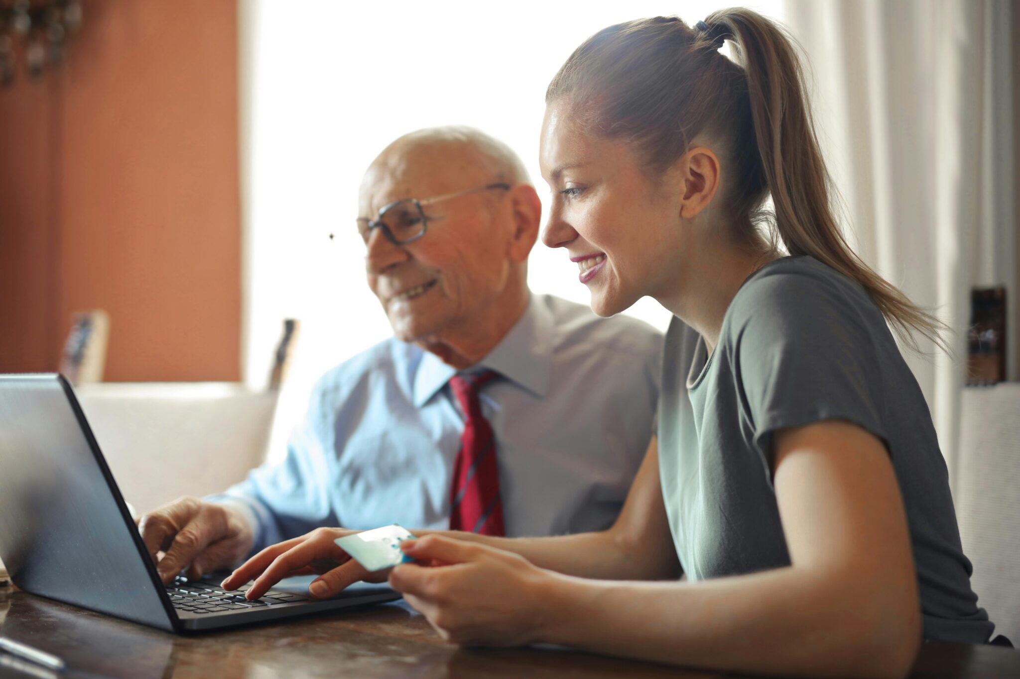 Young lady helping older man with laptop, both smiling